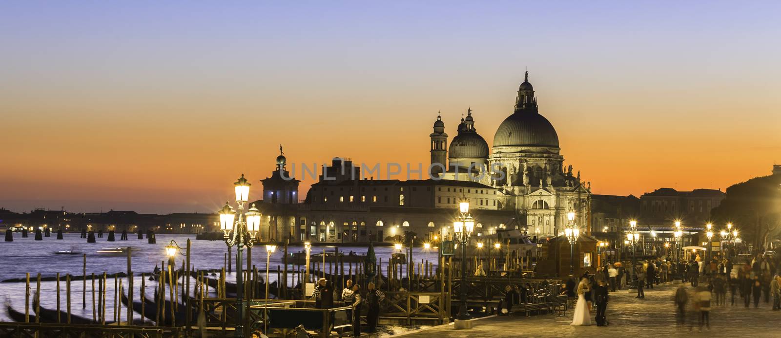 Romantic Italian city of Venice in sunset. World Heritage Site. Traditional Venetian wooden boats, gondolier and Roman Catholic church Basilica di Santa Maria della Salute.