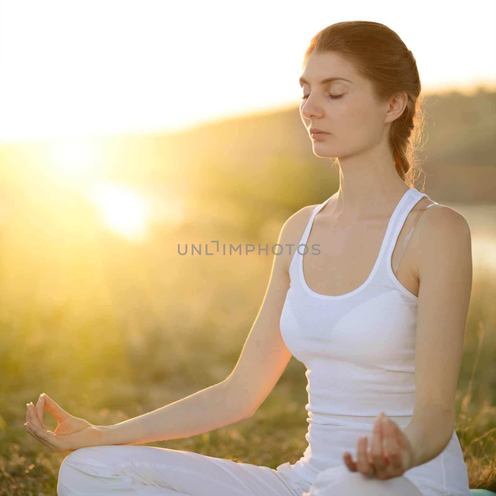 Young Beautiful Woman Practices Yoga on the Sunny Meadow by maxpro