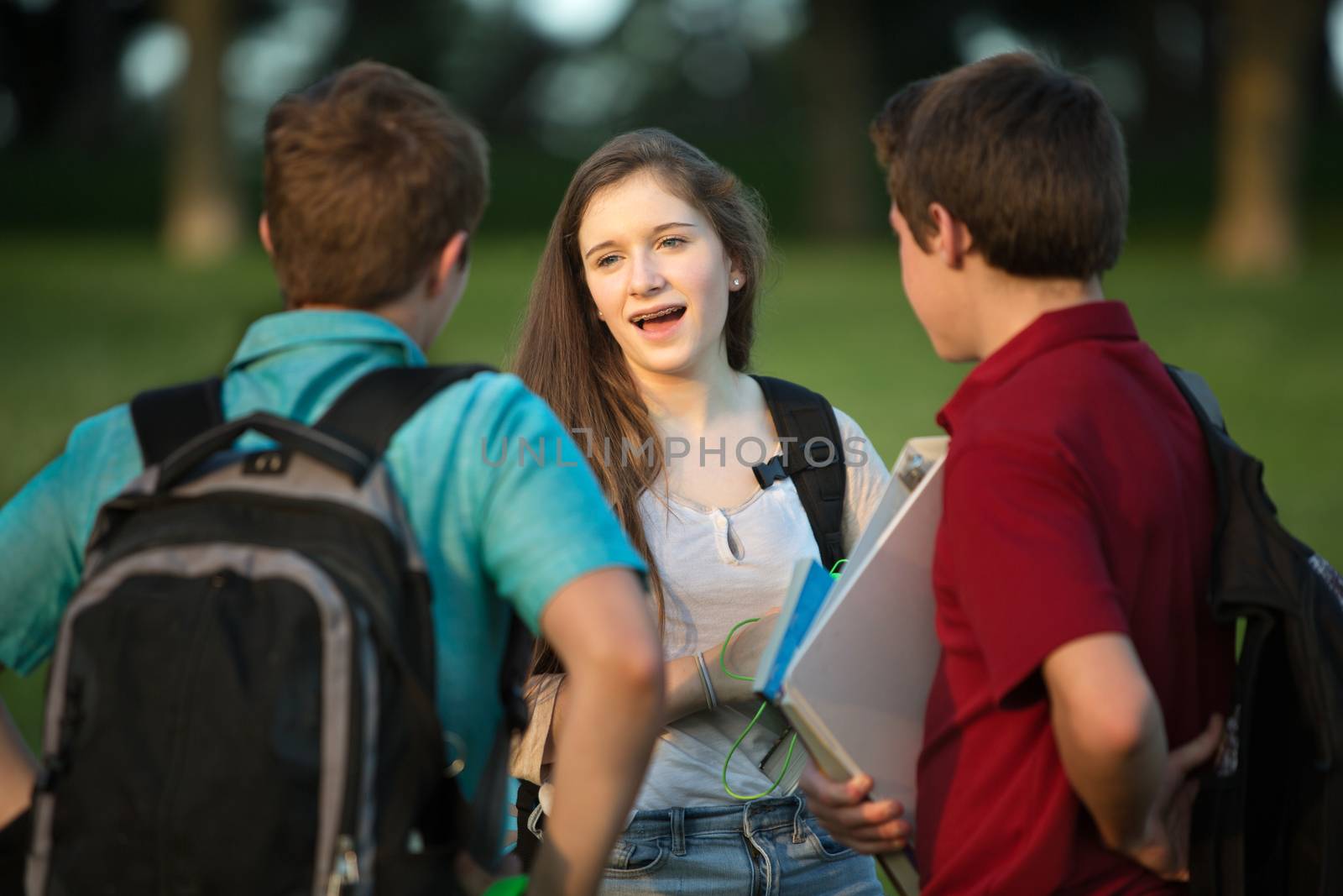 Three friends, girl and boys talking about homework outside