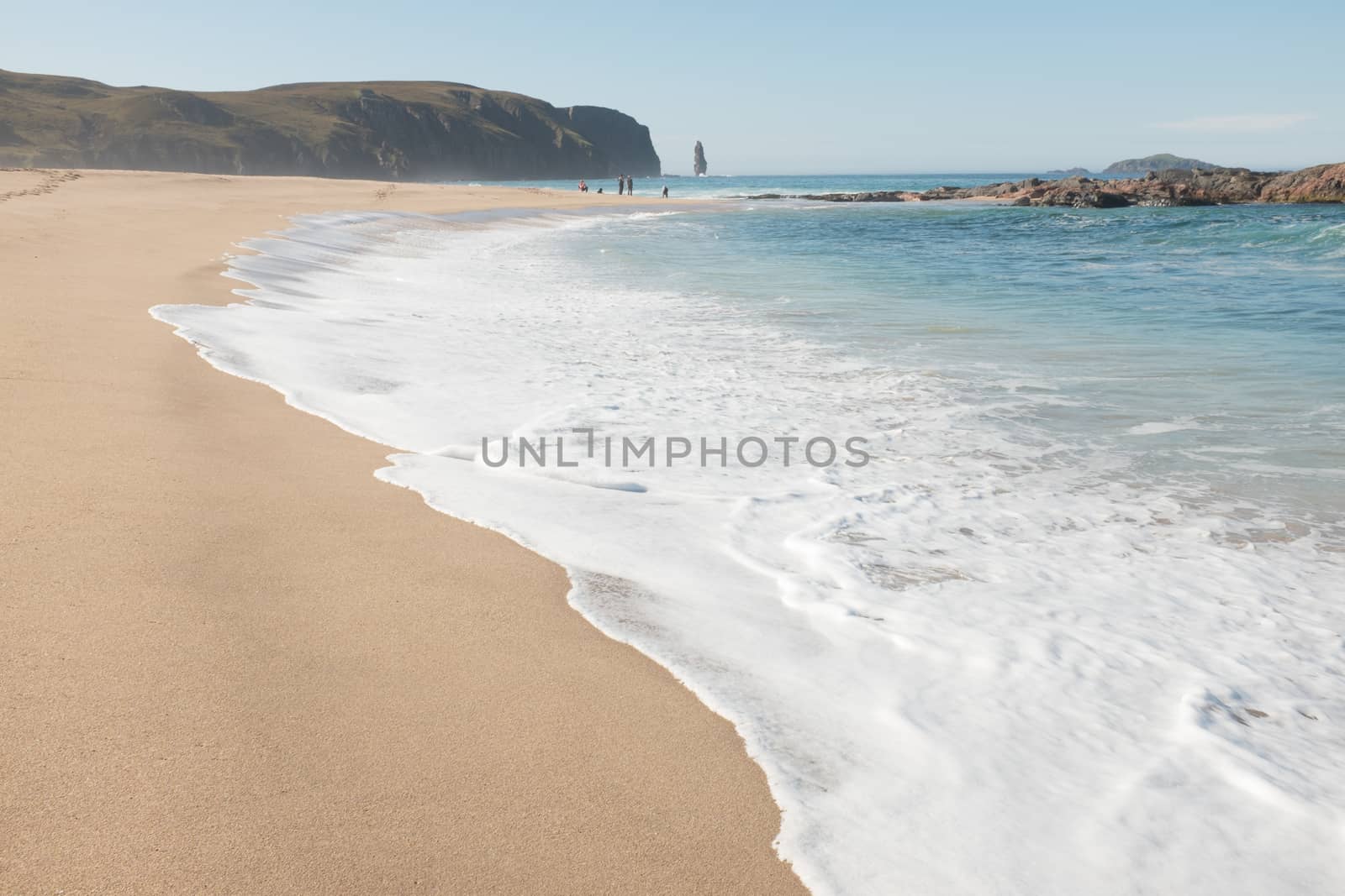 Waves break up the steep white sandy beach with people looking out to the sea-stack off the headland at Sandwood Bay, Sutherland, Scotland, UK.