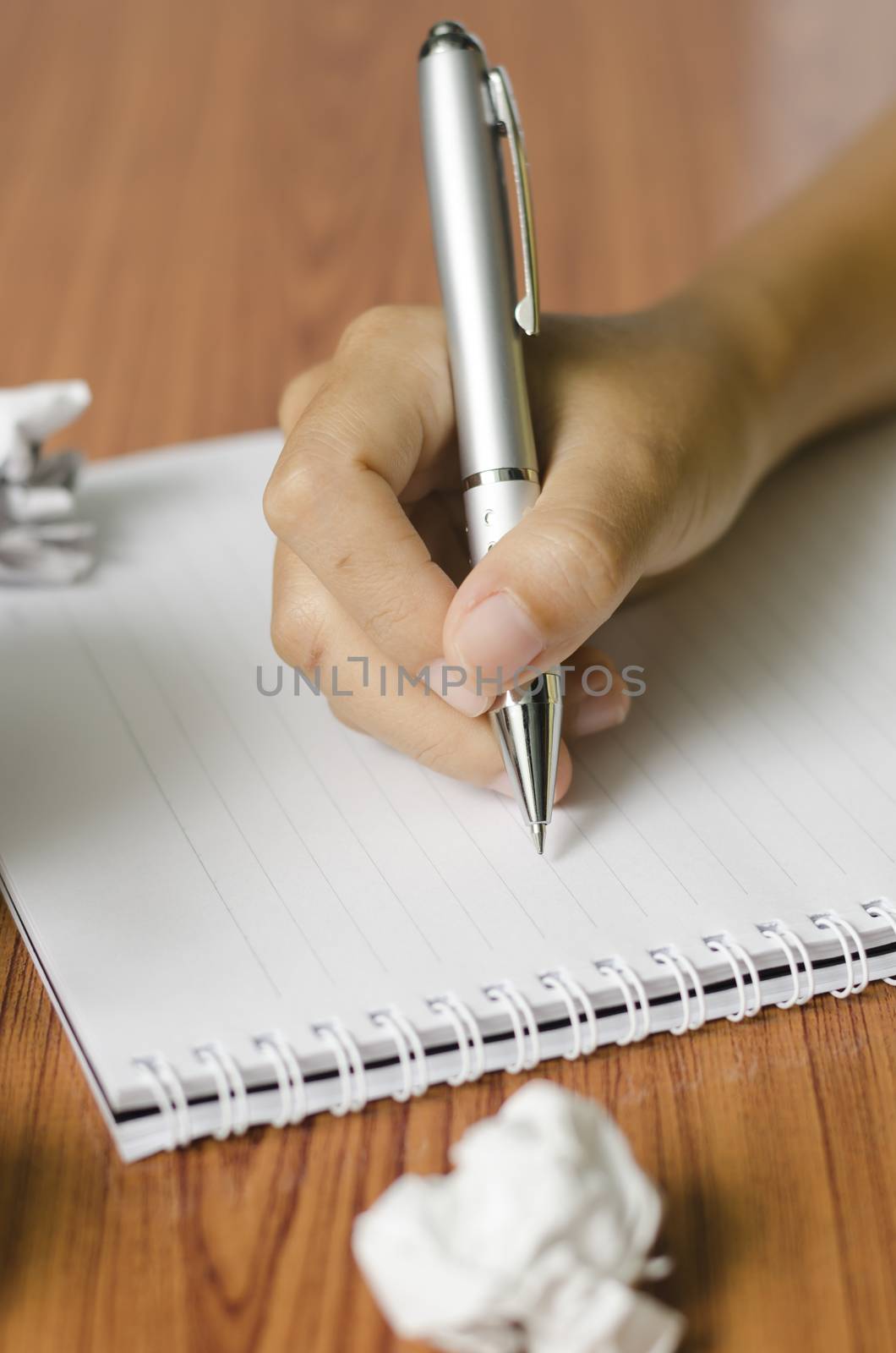 woman hand writing with pen on notebook.there are crumpled paper and coffee cup on wood table background