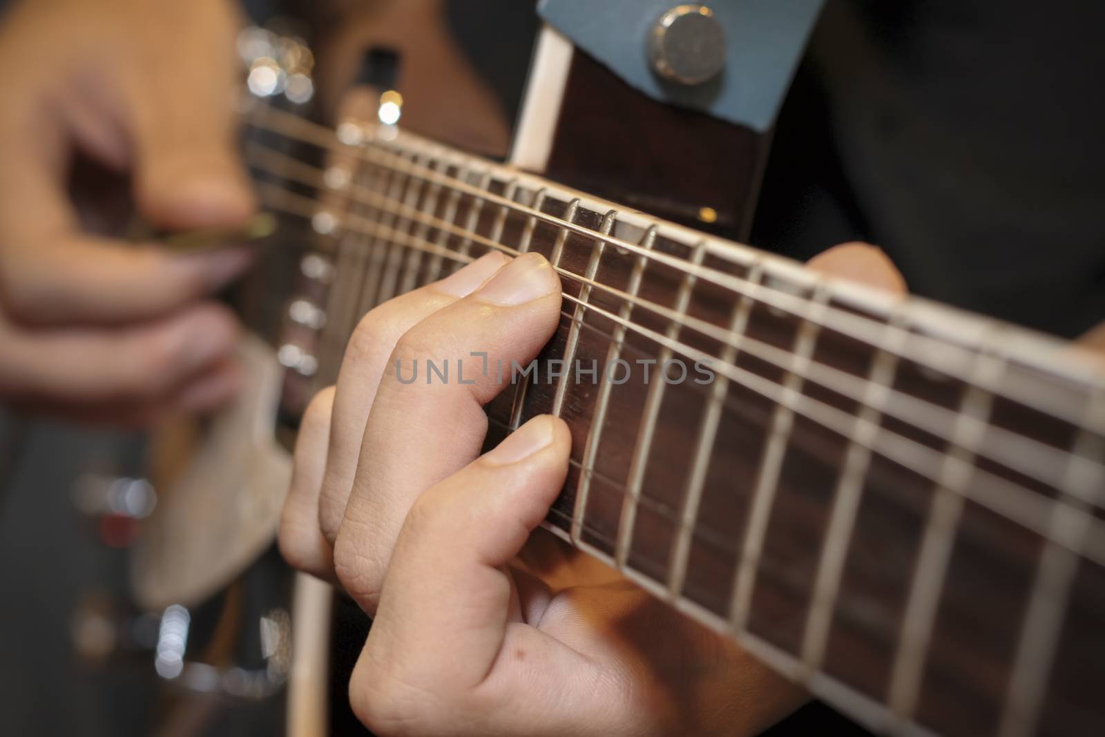 close up shot of a man with his fingers on the frets of a guitar by manaemedia