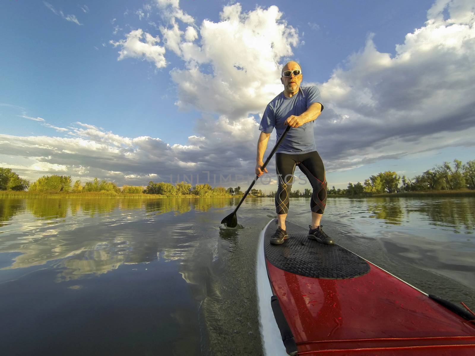 senior male paddler enjoying workout on stand up paddleboard (SUP), calm lake in Colorado, summer