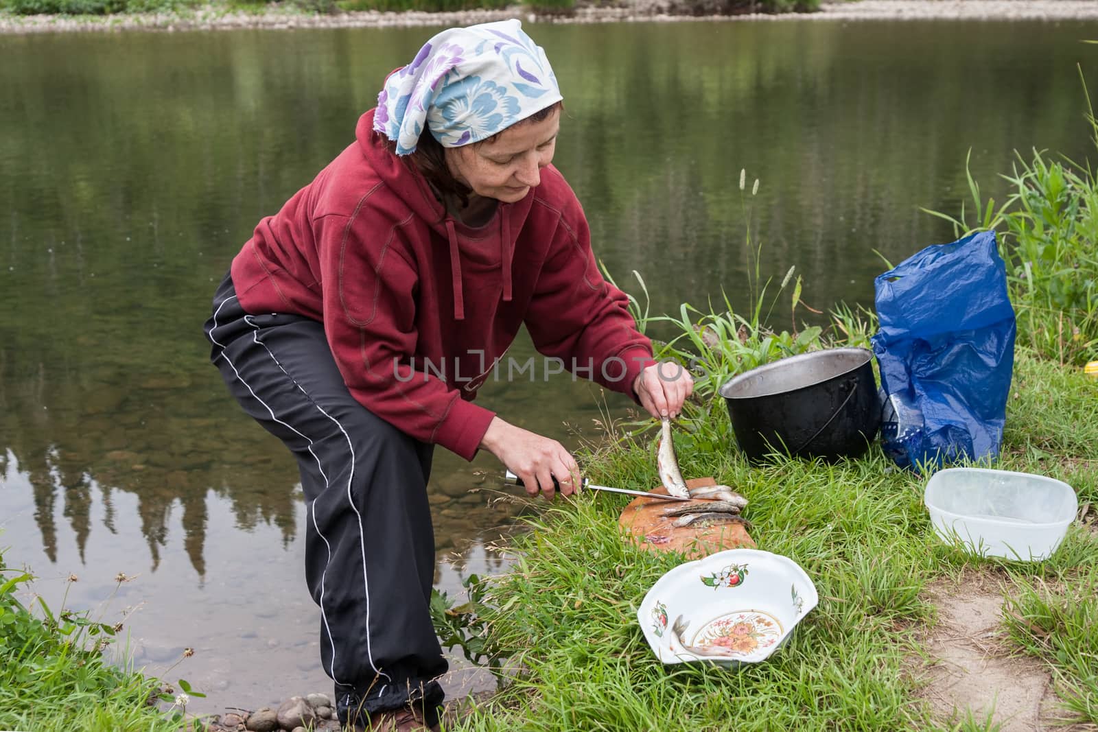A woman cleans a fish on the river bank