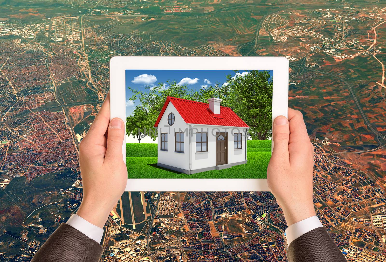 Hands holding tablet pc with image of house on the screen. Aerial view of cityscape