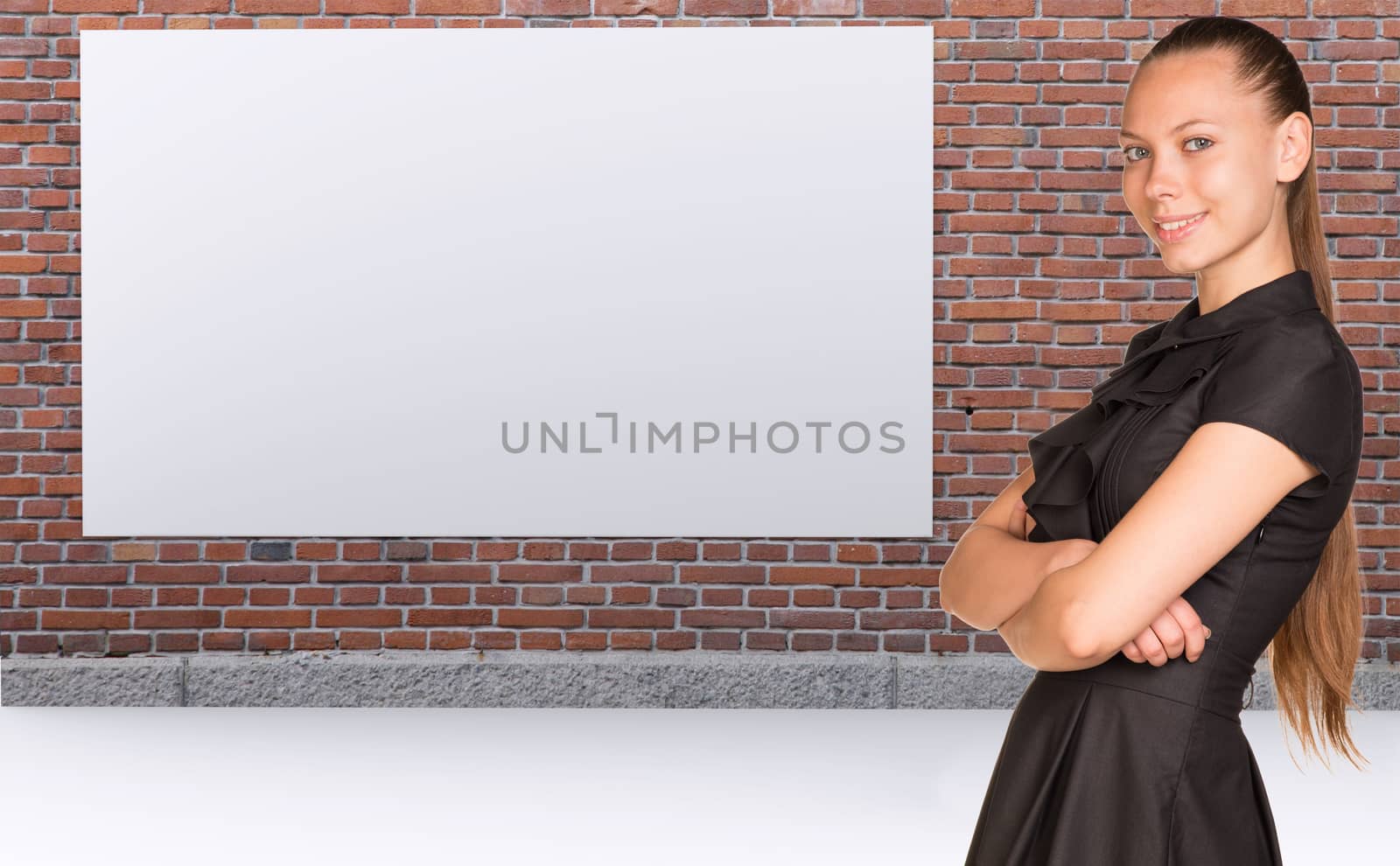 Businesswoman standing with crossed arms. Brickwall with empty billboard as backdrop