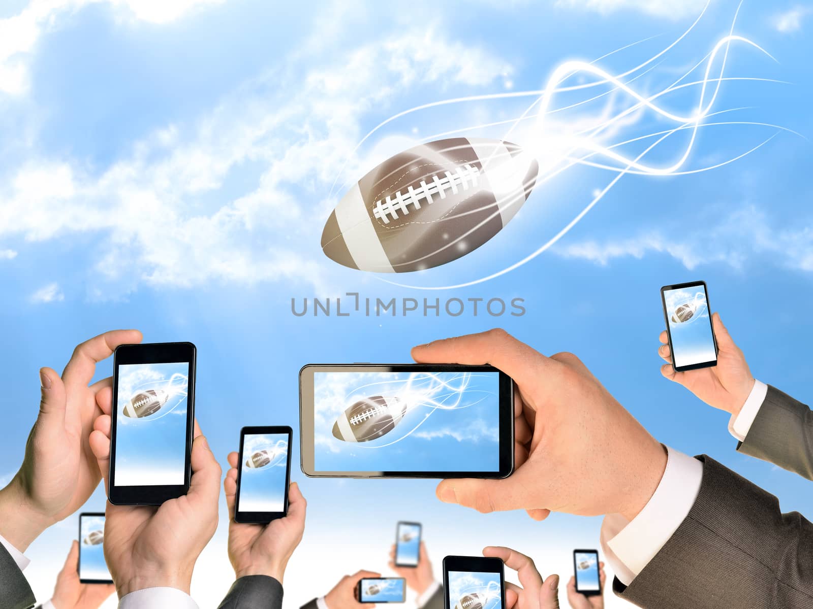 Hands holding smart phones and shoot video as falling American football. Sky with clouds on background