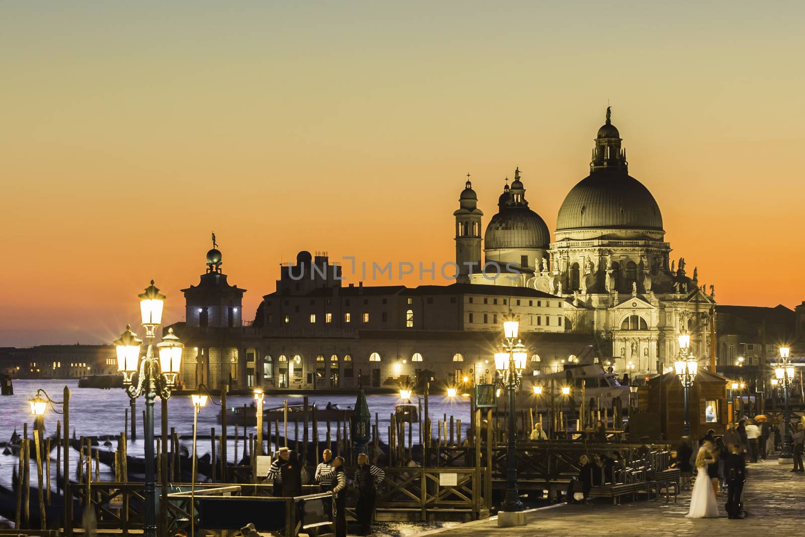 Romantic Italian city of Venice in sunset. World Heritage Site. Traditional Venetian wooden boats, gondolier and Roman Catholic church Basilica di Santa Maria della Salute.
