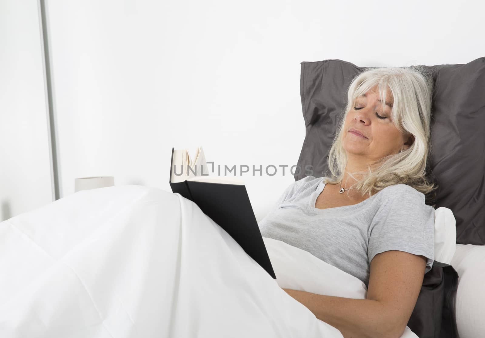 Woman with closed eyes and a book in bed
