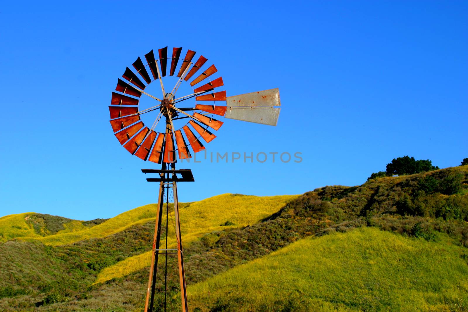 Water pumping windmill with a hill and blue sky in the background.
