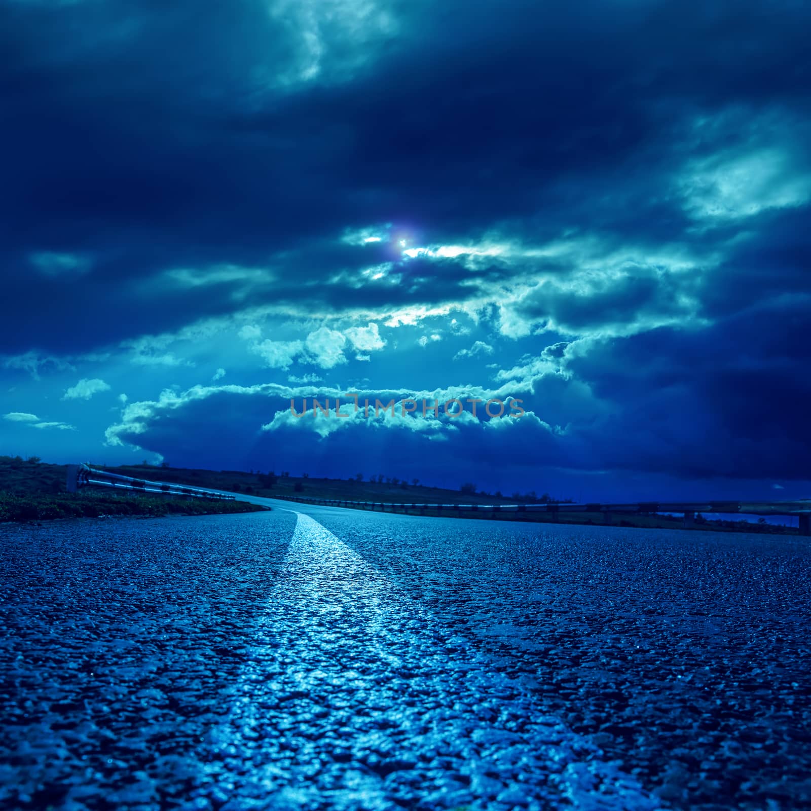 low dramatic clouds over asphalt road in dark blue moonlight