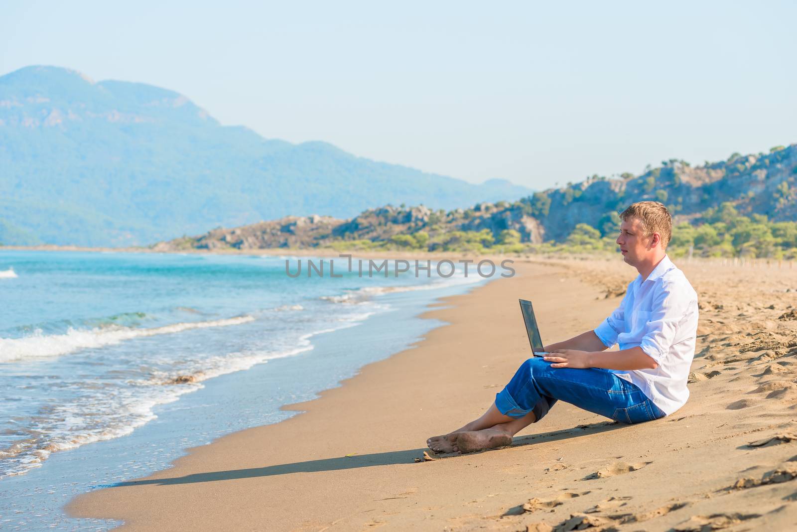 handsome young man with a laptop sitting on the beach