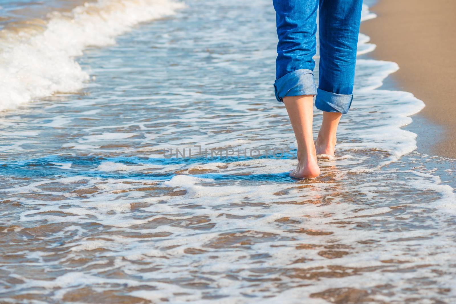 male legs in jeans walking along the sandy seashore