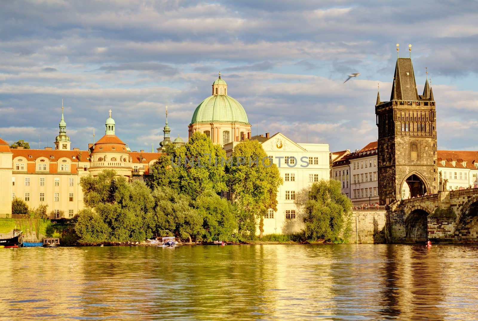 Photo shows the bridge, river and some old houses in Prague.