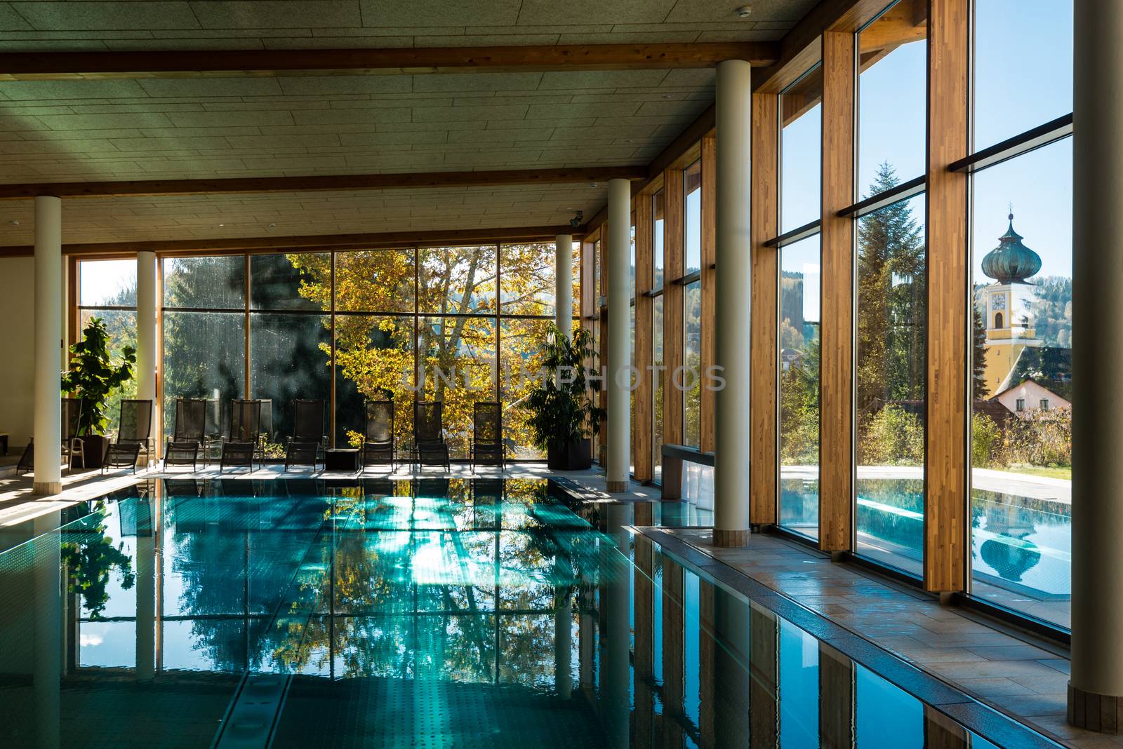 view of indoor and outdoor pools of a hotel with reflections and a church tower in the distance in autumn