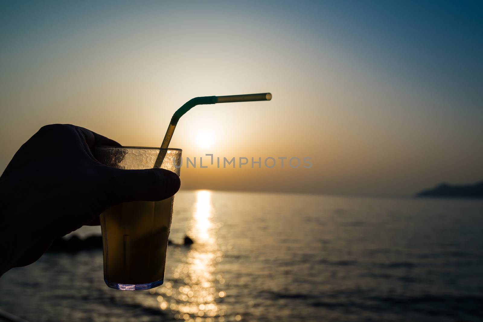 hand holding a cocktail with a straw during sunset on the beach
