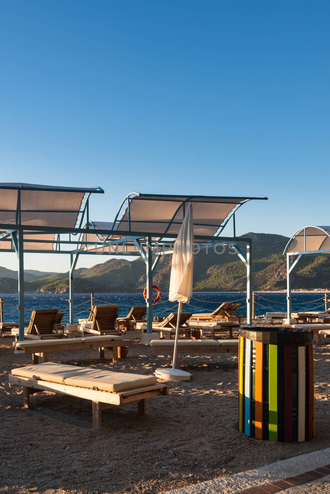 Sun loungers with umbrellas and colorful garbage can on the beach