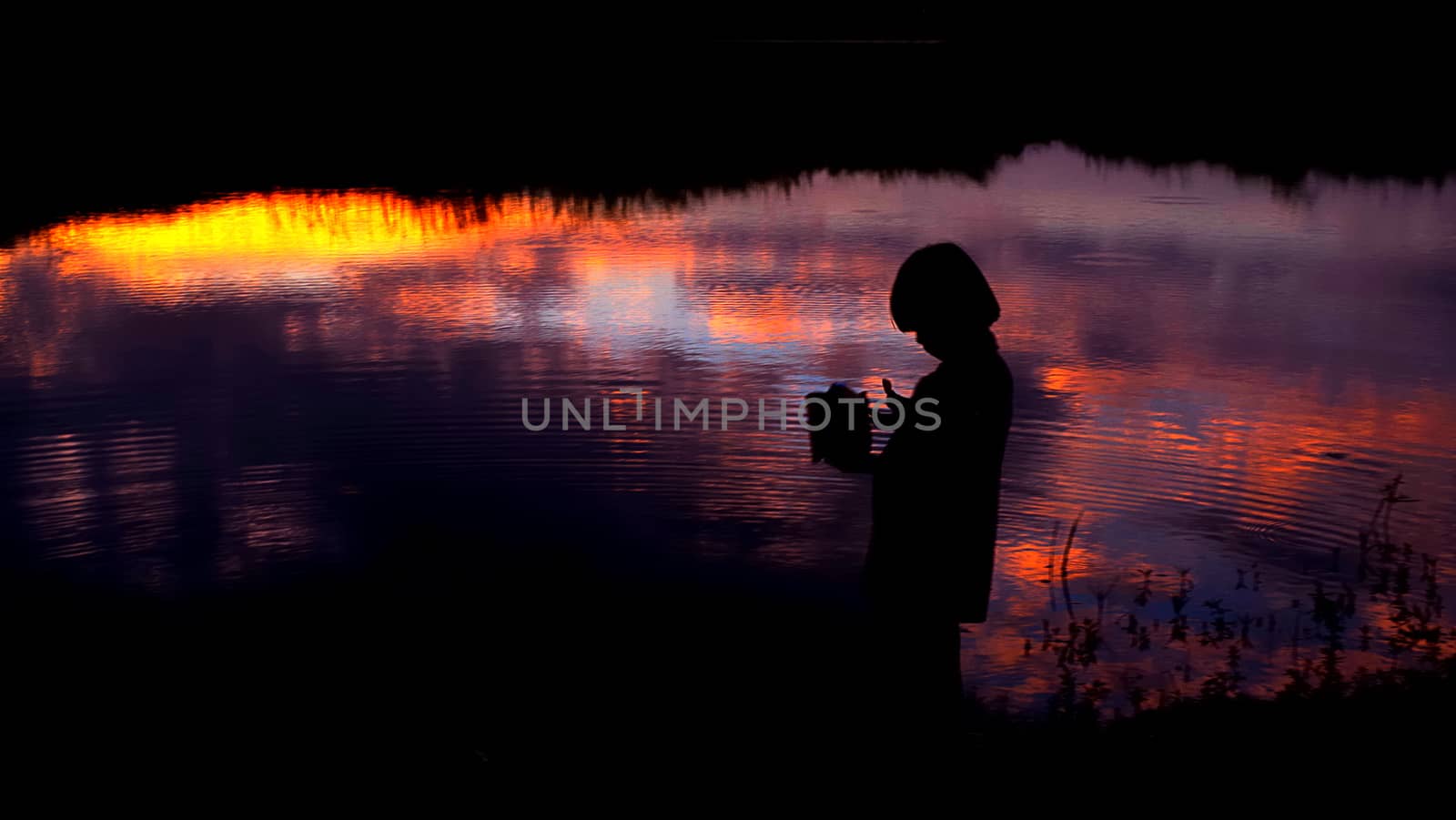 Silhouette of child beside the swamp with sunset sky reflected