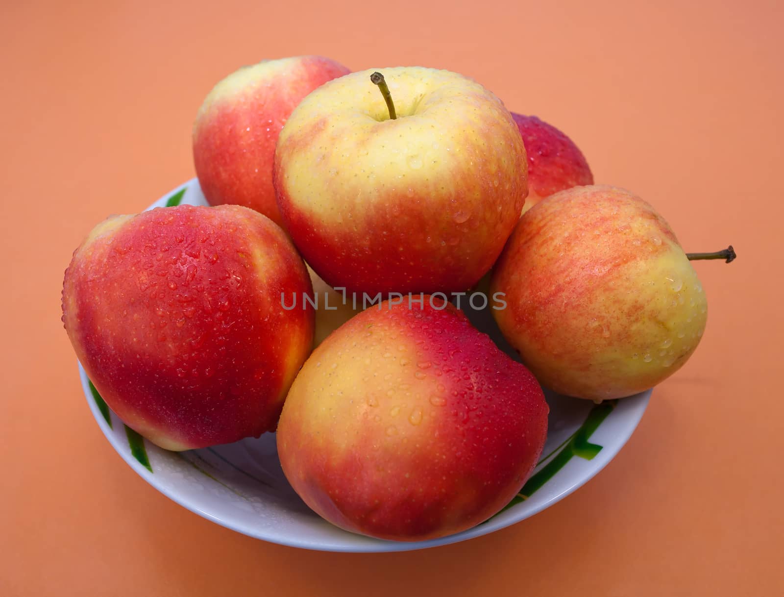Red and yellow apples with kalyami water on their surface in the plate on an orange background