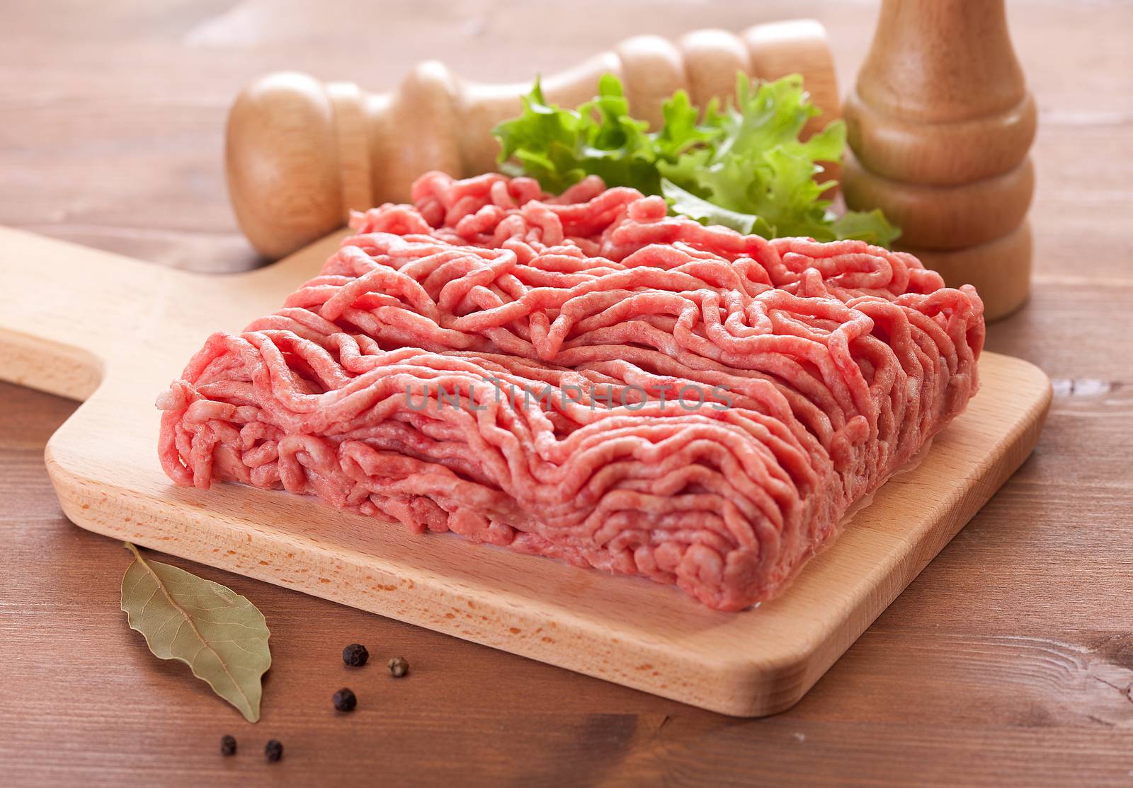 Fresh minced meat on the wooden board with lettuce, bay leaf and pepper on the table