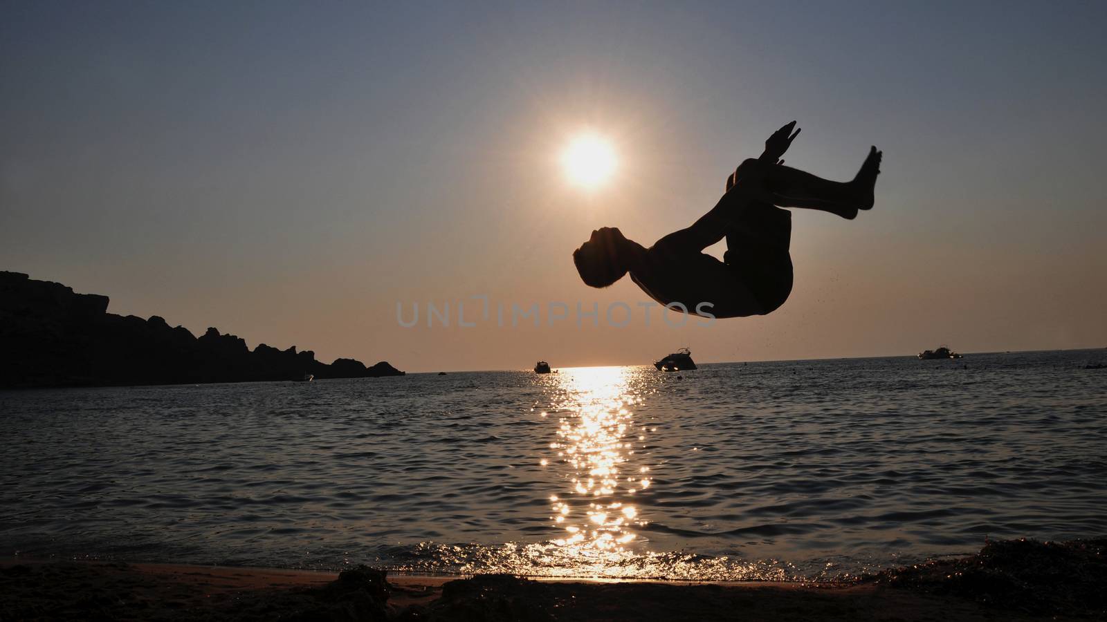 A boy jumping backflip in front of the sea during sunset