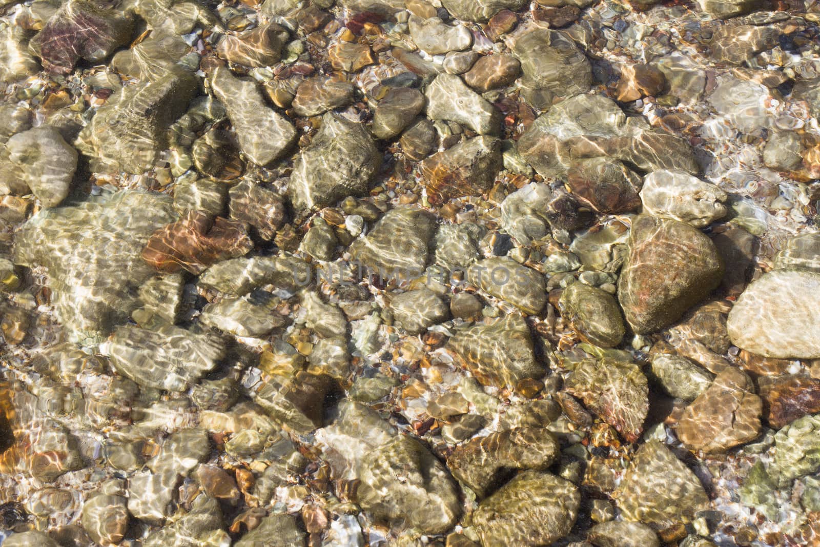pebbles under water with the sun reflected in water
