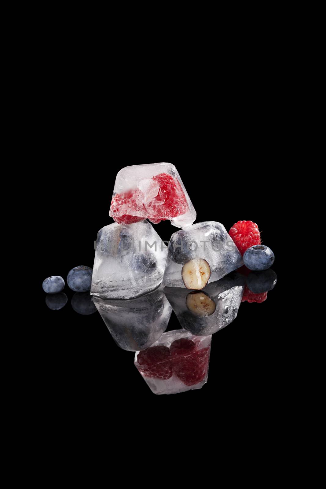 Blueberries and raspberries frozen in ice cubes black background. Fresh fruit eating. 