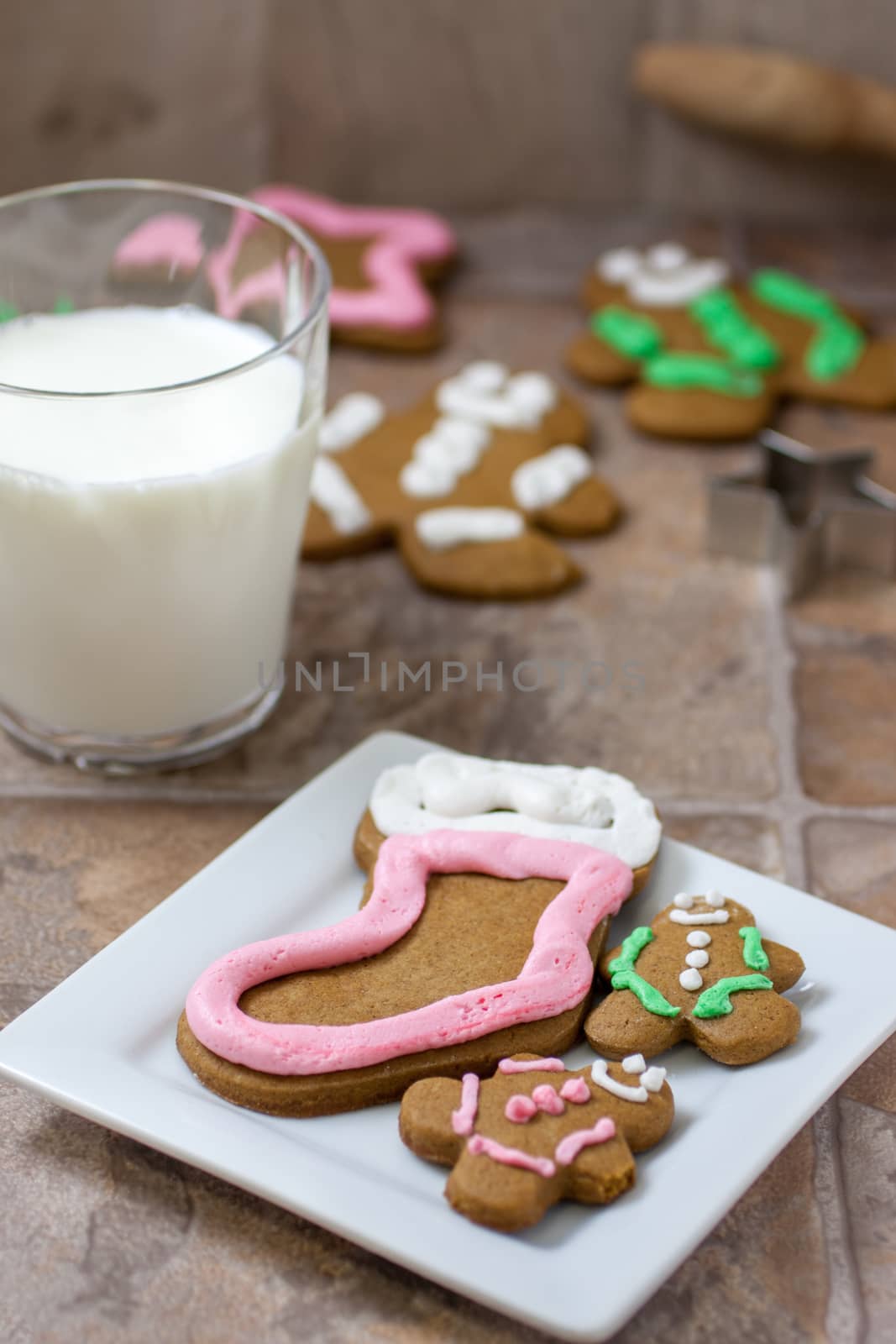 Several gingerbread Christmas cookies on a white plate with cookie cutters, a rolling pin, and several cookies in the background.