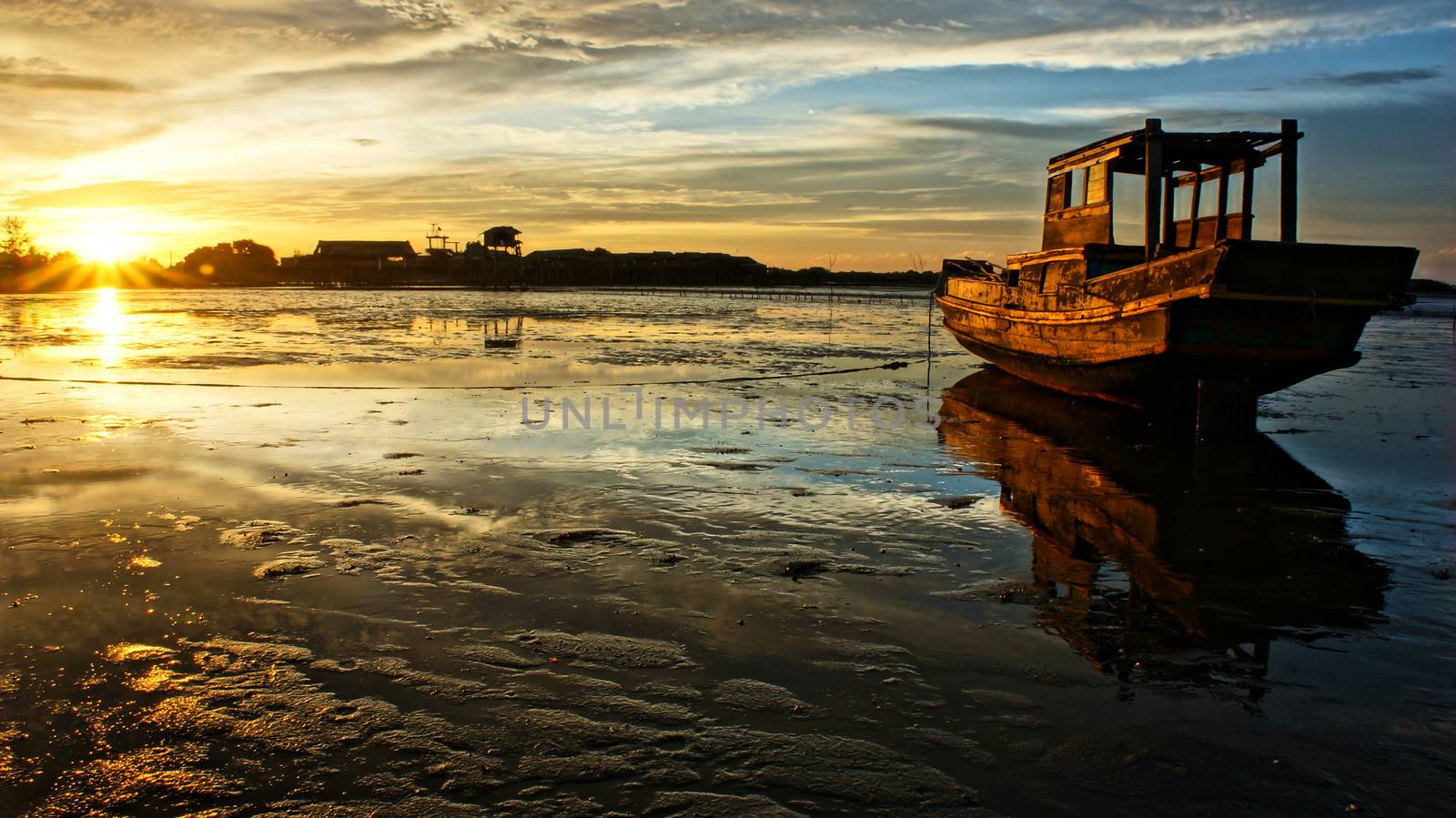 Abstract landscape of sea when sunset, tide going out, sun go down, sunbeam shine on wooden fishing boat that reflect on surface water of beach, colorful sky at evening scene 