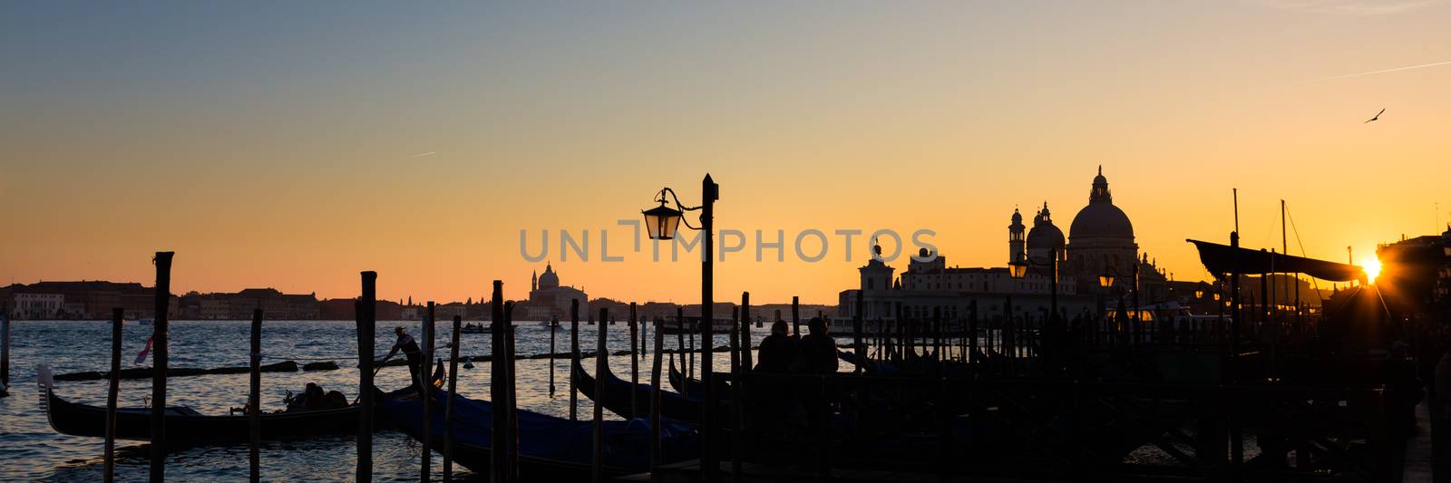 Romantic Italian city of Venice in sunset. World Heritage Site. Traditional Venetian wooden boats, gondolier and Roman Catholic church Basilica di Santa Maria della Salute.