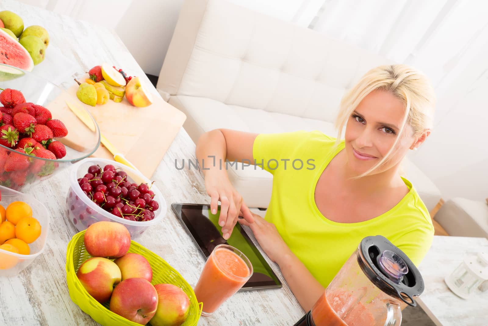 A beautiful mature woman with a smoothie in the kitchen using a tablet.
