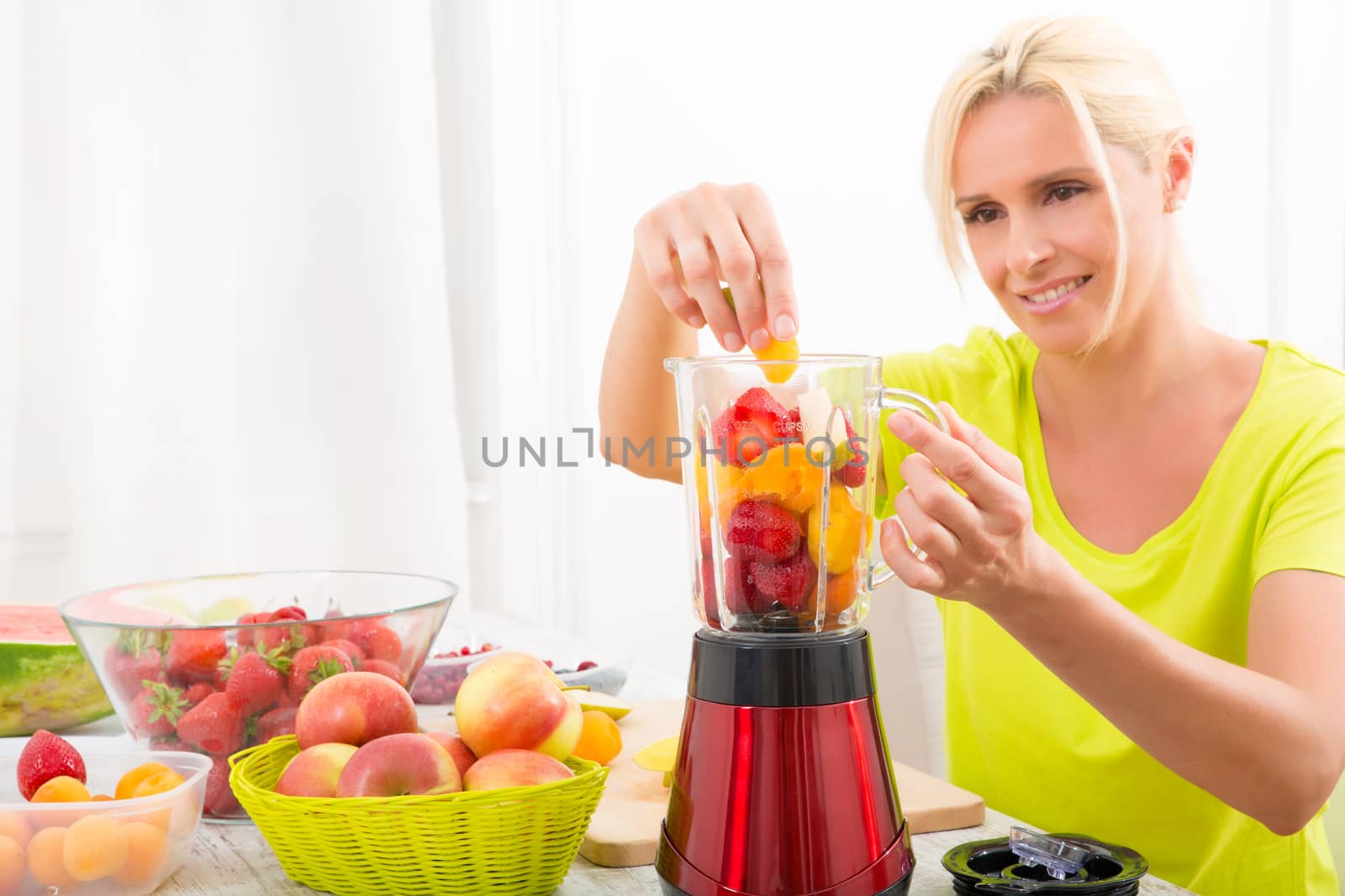 A beautiful mature woman preparing a smoothie or juice with fruits in the kitchen.
