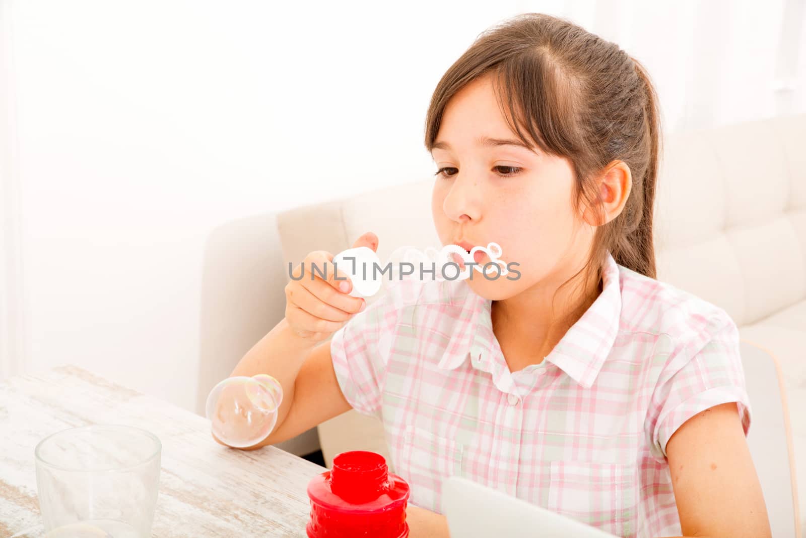 Portrait of girl blowing bubbles at home at the table.
