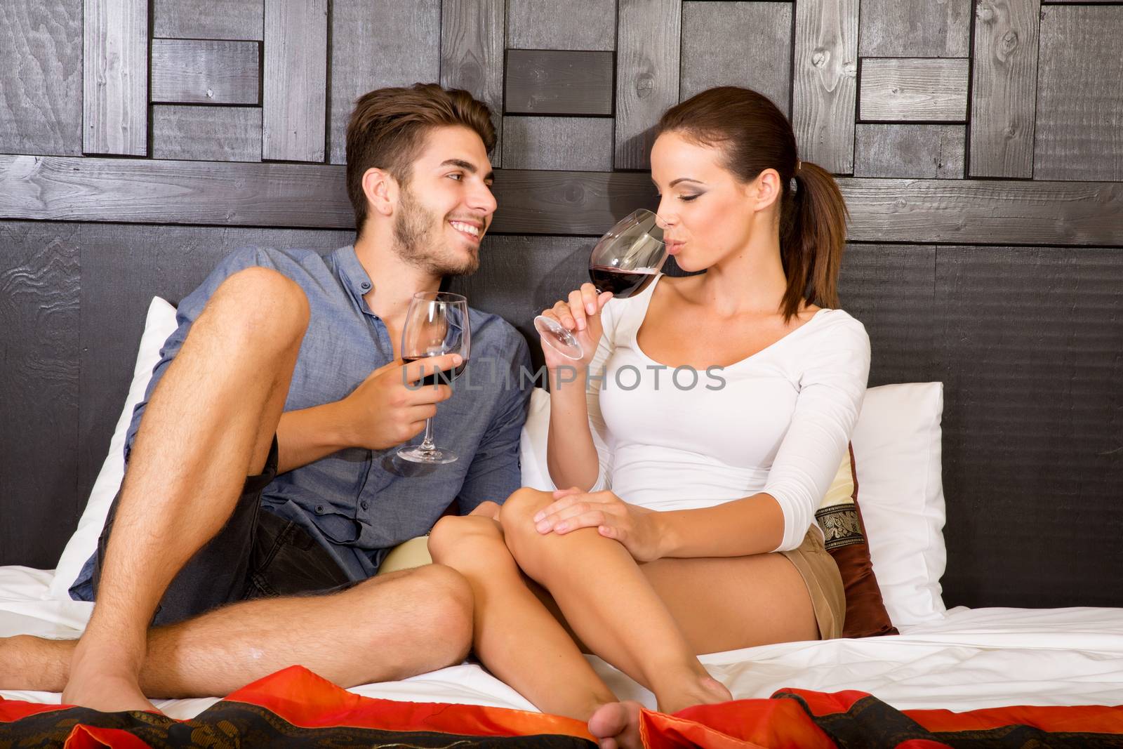 A happy young couple on their vacations with a glass of wine lying on the bed in an asian style hotel room.
