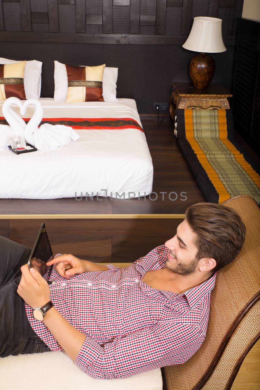 A young man using a tablet pc in a asian hotel room.	
