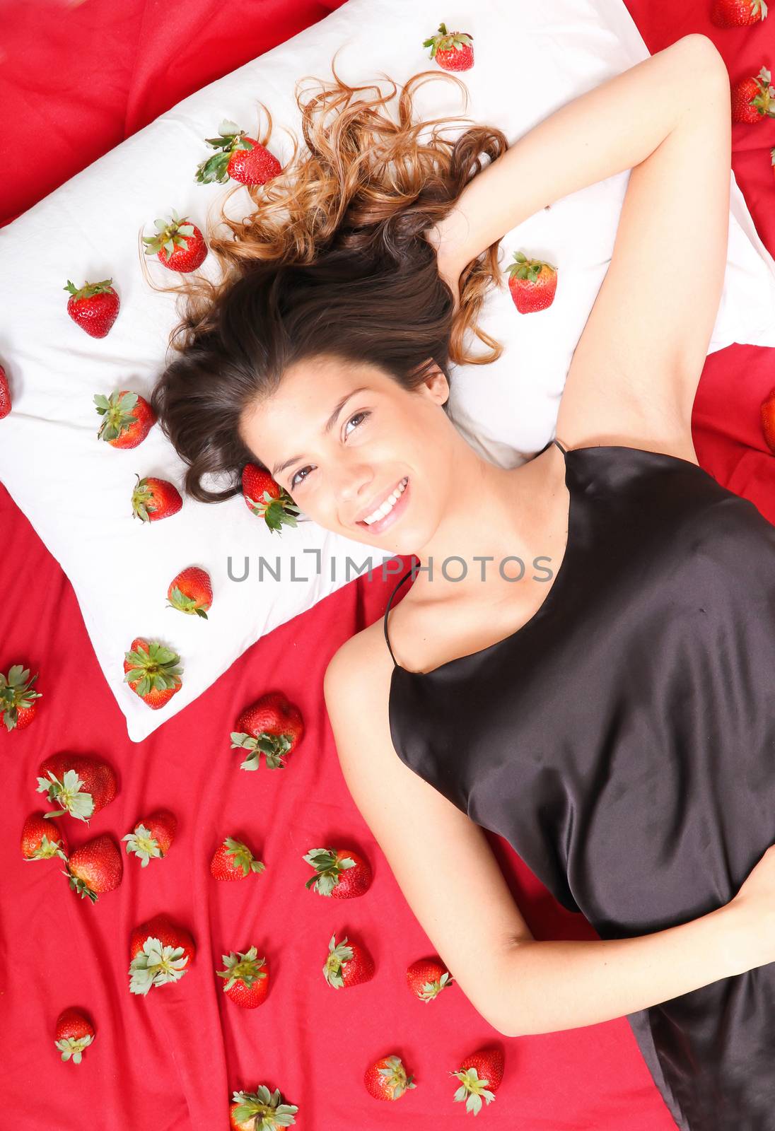 A young adult american woman smiling in a bed full of strawberries.
