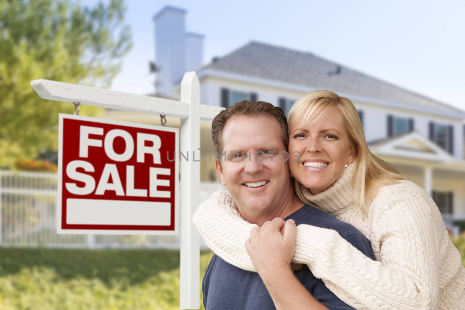 Affectionate Happy Couple in Front of New House and For Sale Real Estate Sign.