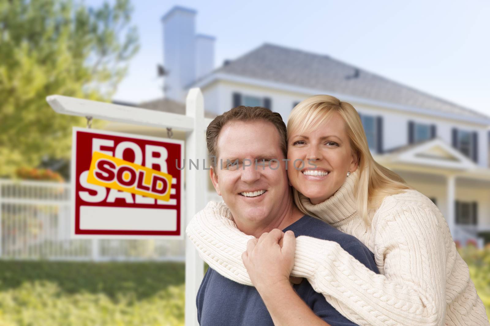 Affectionate Happy Couple in Front of New House and Sold For Sale Real Estate Sign.