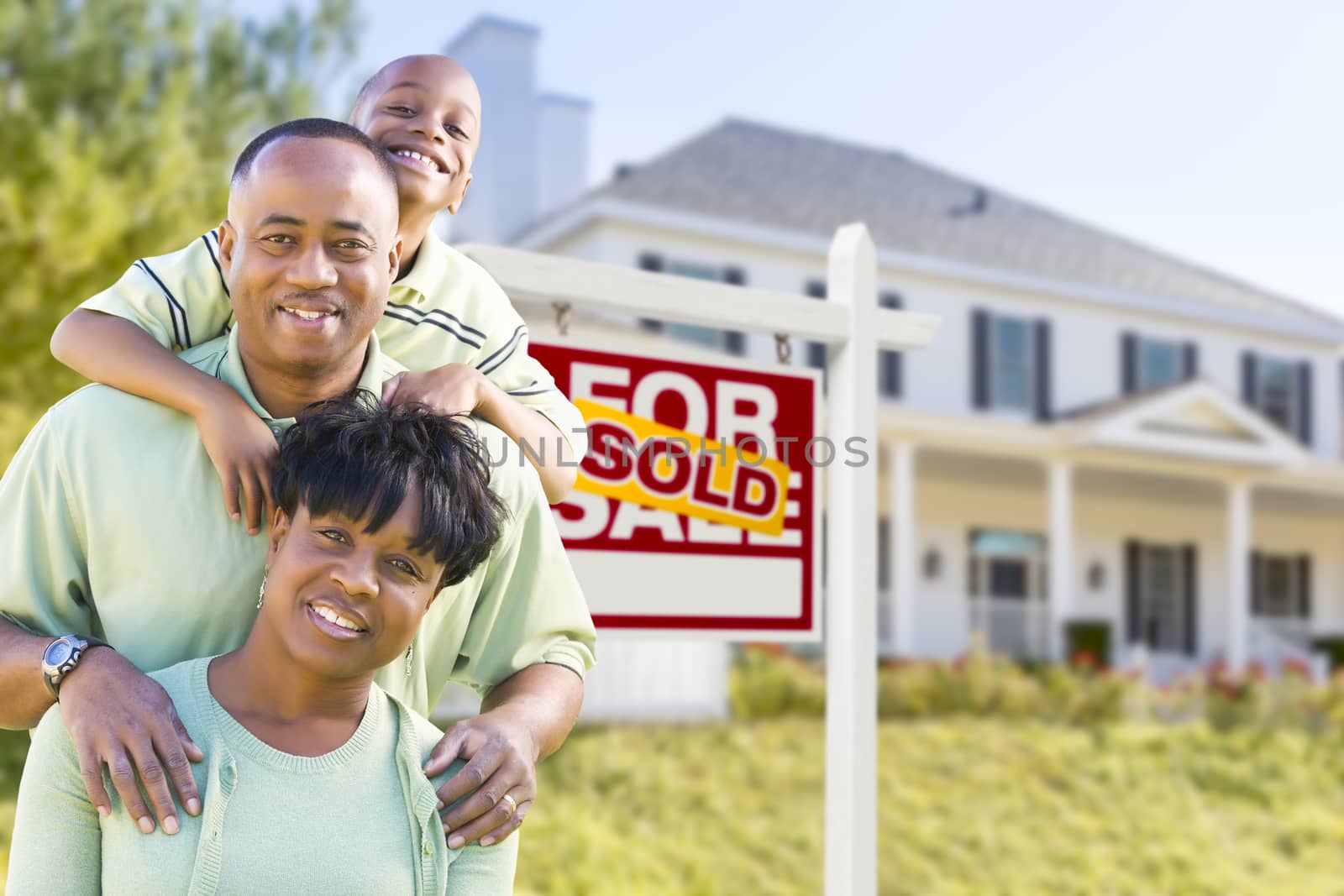 Happy African American Family In Front of Sold For Sale Real Estate Sign and House.