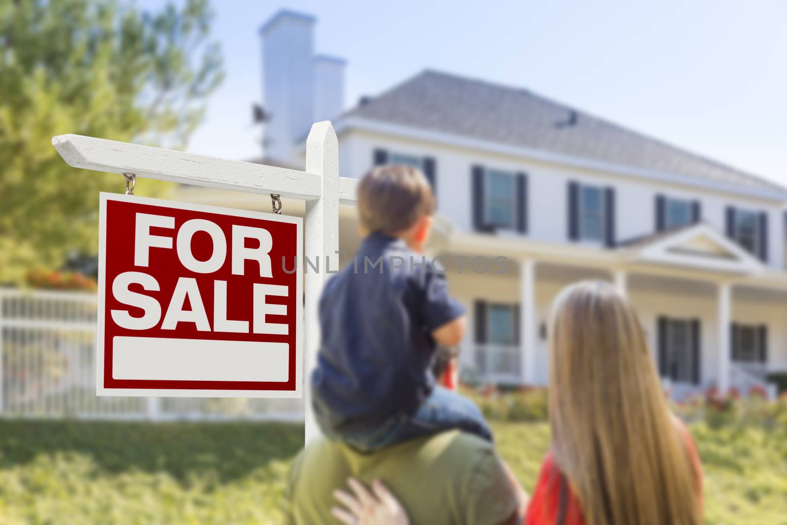 Curious Family Facing For Sale Real Estate Sign and Beautiful New House.