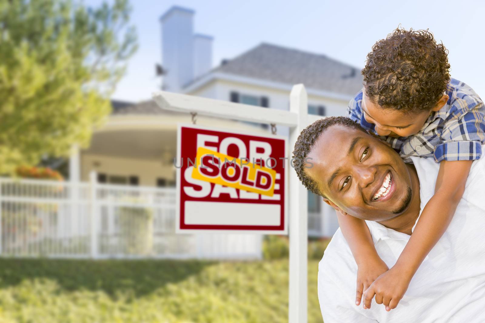 Happy African American Father and Mixed Race Son In Front of Sold Home For Sale Real Estate Sign and New House.