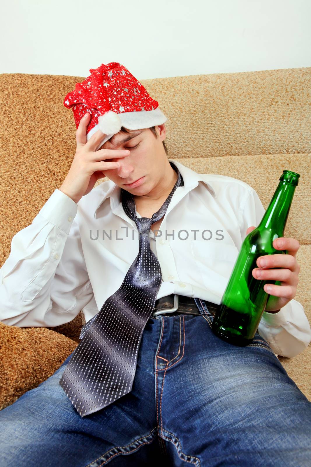 Drunken Teenager in Santa Hat sleeping on the Sofa at the Home with the Beer