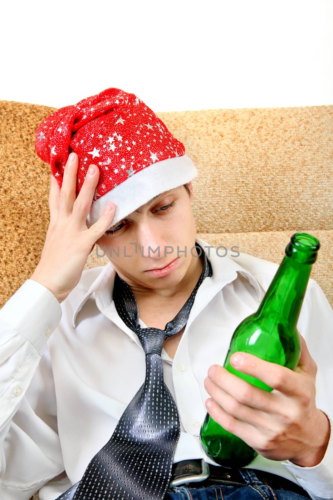 Sad and Tired Teenager with Bottle of the Beer and Santa Hat on the Sofa at the Home