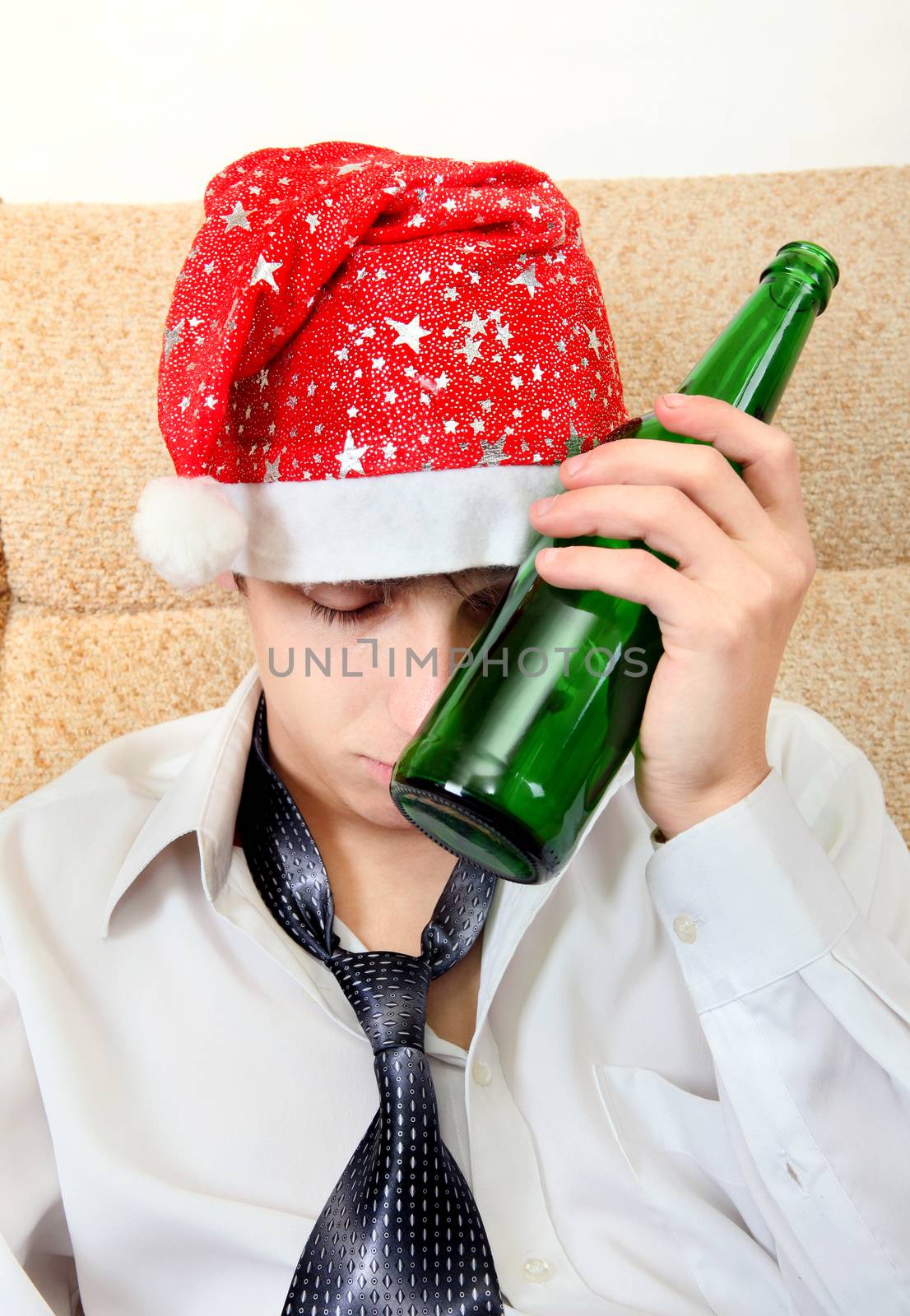 Sad and Tired Teenager with Bottle of the Beer and Santa Hat on the Sofa at the Home