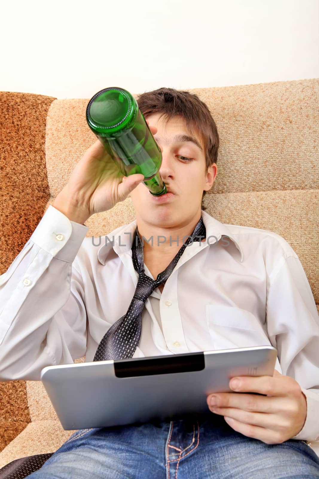 Teenager drinks a Beer with Tablet Computer on the Sofa at the Home