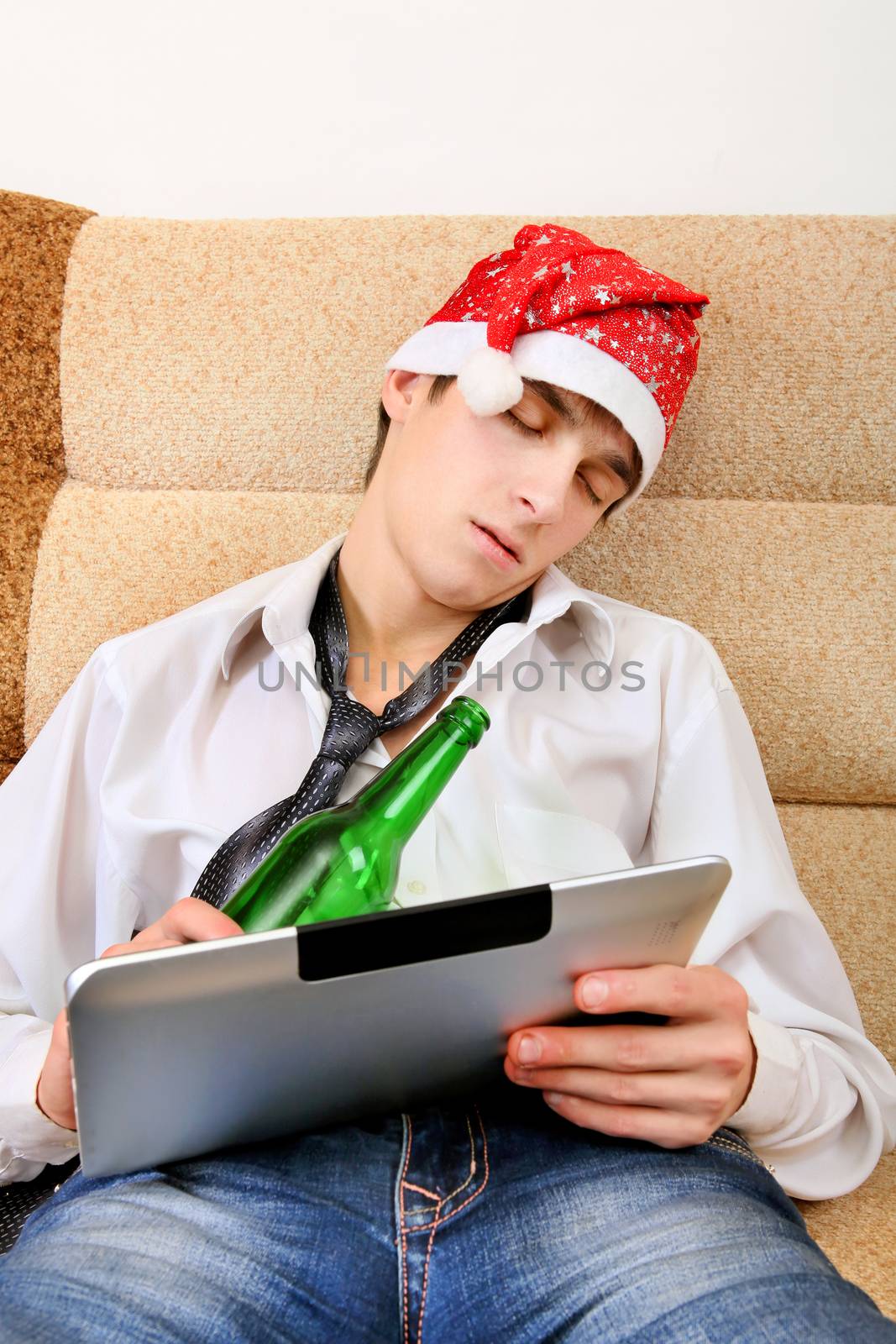 Tired Teenager sleeping in Santa Hat with Tablet Computer and Bottle of the Beer at the Home