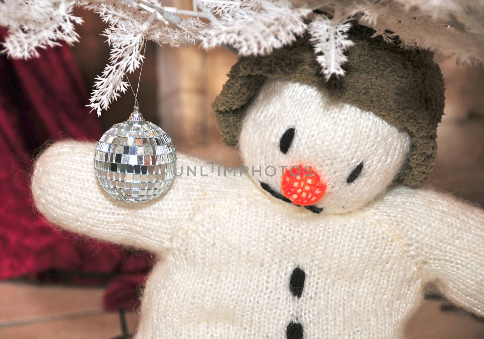 Snowman toy in green hat  holding disco ball under the white tree