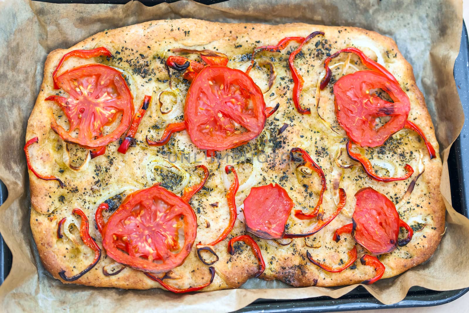 Delicious fresh traditional Italian focaccia bread with tomatoes, red peppers, onions, basil and olive oil on cooking pan