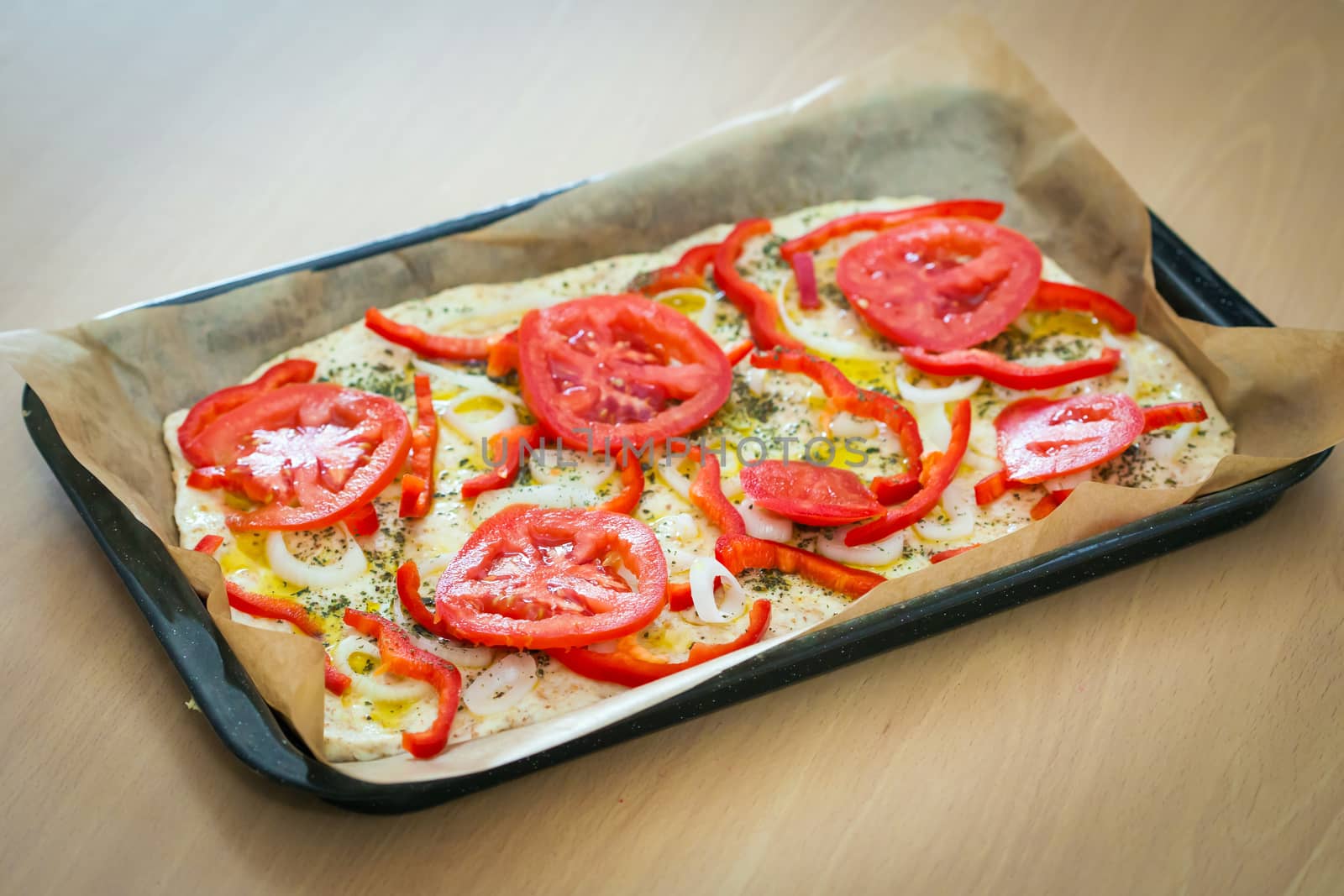 Delicious fresh traditional Italian focaccia bread with tomatoes, red peppers, onions, basil and olive oil on pan ready to cook