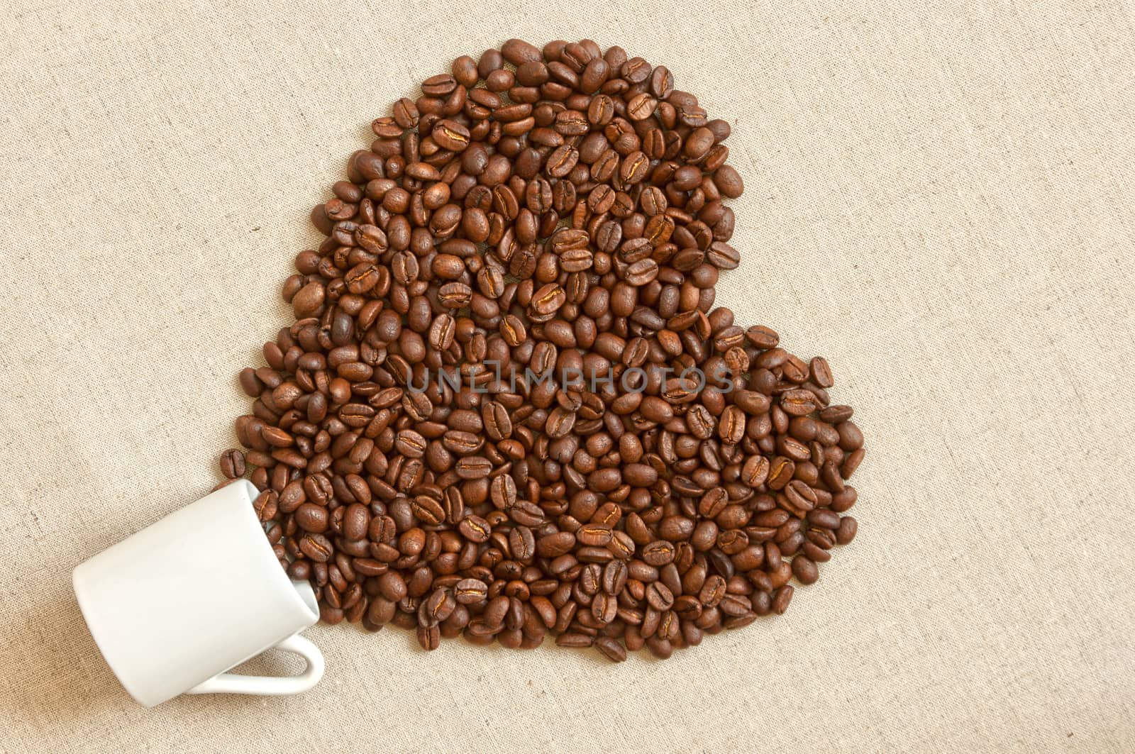Love shaped coffee beans spilled out of cup of linen fabric
